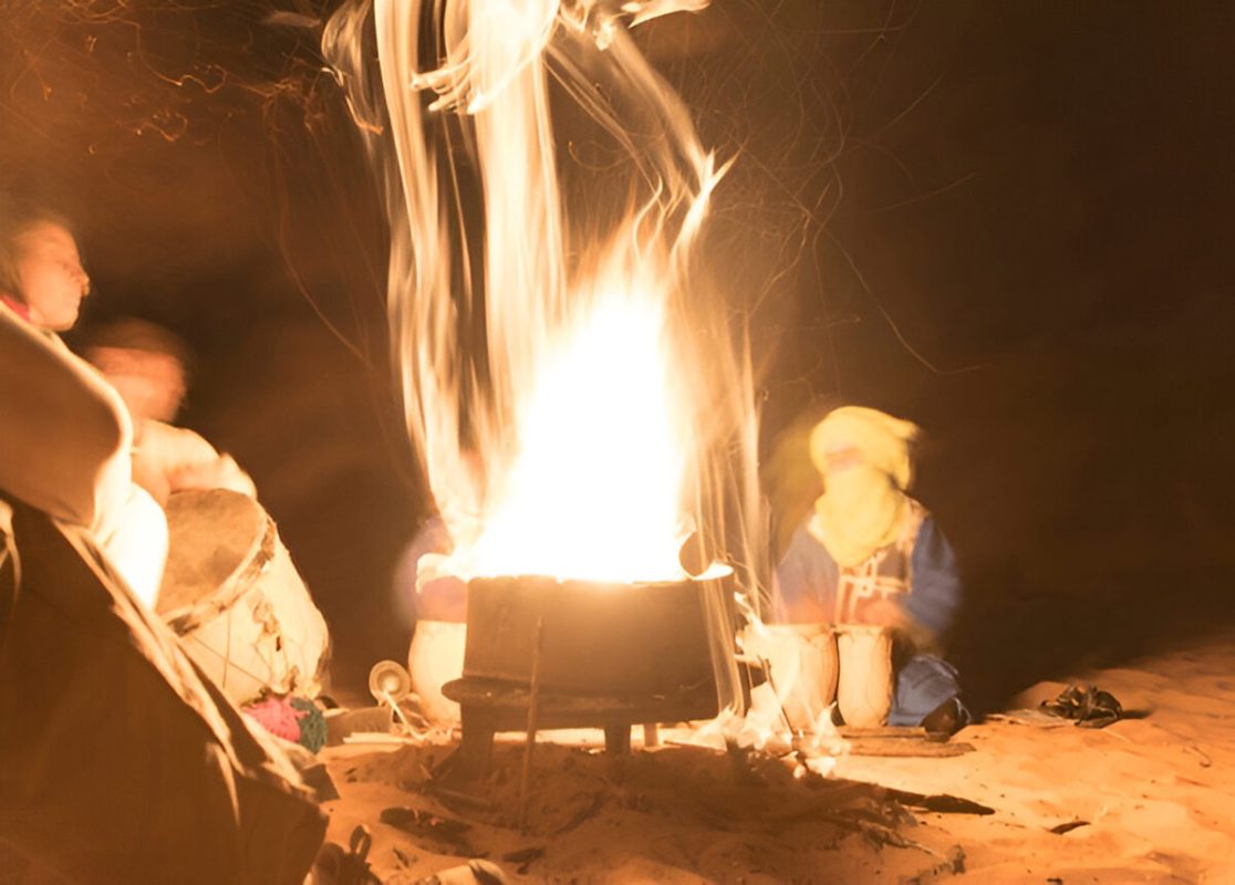 Travelers enjoying traditional Berber drumming around a campfire during a 2-Day Desert Adventure Zagora under the starry Sahara night sky.