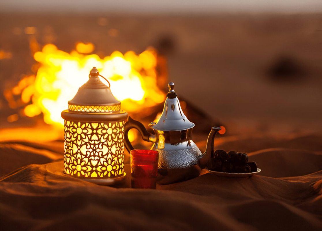 Traditional Moroccan tea set, lantern, and dates beside a glowing campfire at sunset during the 2-Day Desert Adventure Zagora.