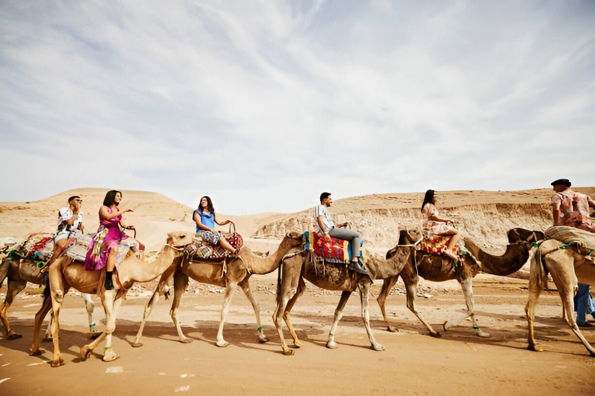 Small group of 5–6 travelers riding camels in the rocky Agafay Desert near Marrakech Morocco