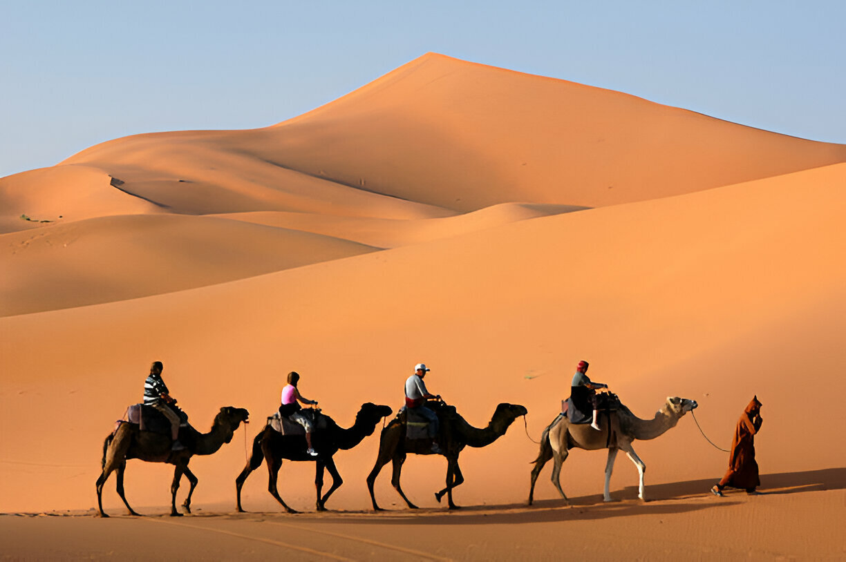 Group of six travelers riding camels in the Sahara Desert during a shared 3-day tour from Marrakech to Fes Morocco