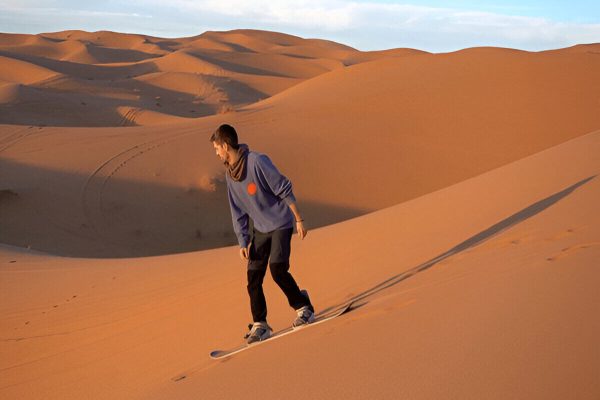 Boy sandboarding on the large Erg Chigaga sand dunes during a 3-day Marrakech desert tour