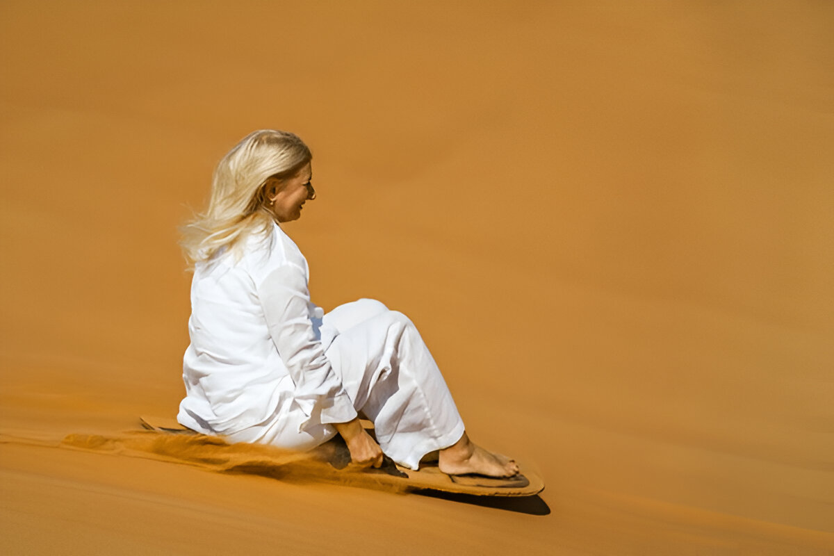 Client enjoying sandboarding on the Erg Lihoudi dunes during a tour from Zagora
