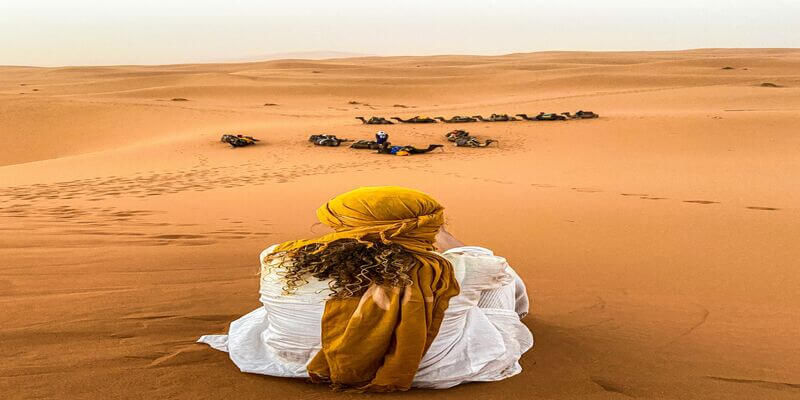 Traveler sitting in the golden Sahara dunes during a shared desert tour