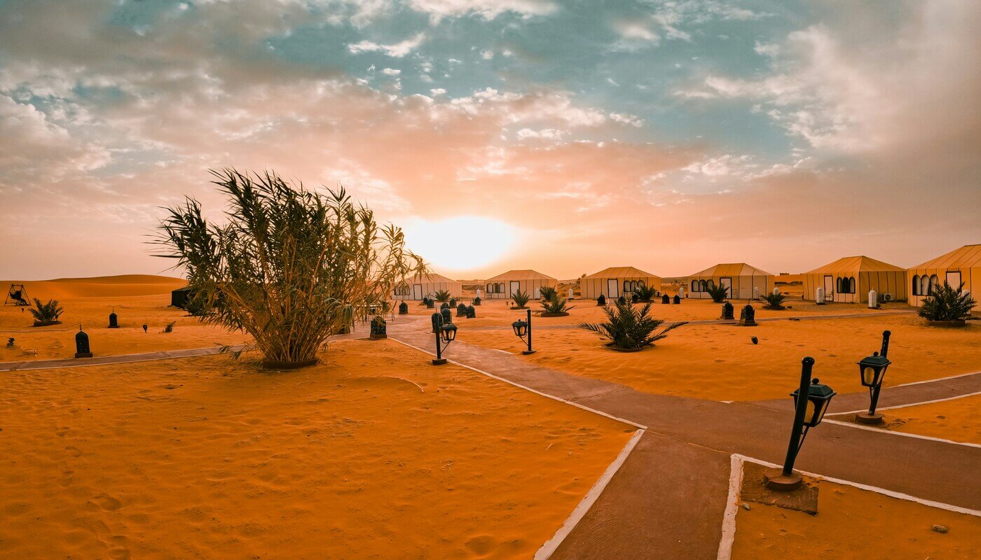 Luxury desert camp in Morocco surrounded by golden dunes at sunset