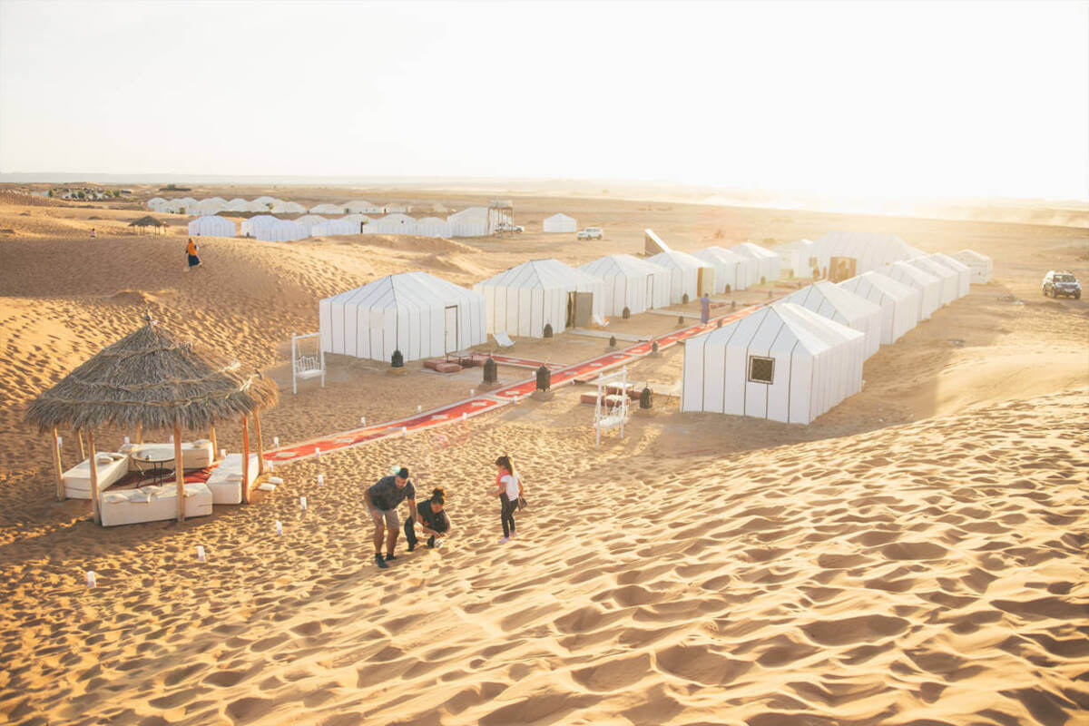 Golden dunes of Erg Chebbi in Merzouga with camels and a luxury desert camp at sunset